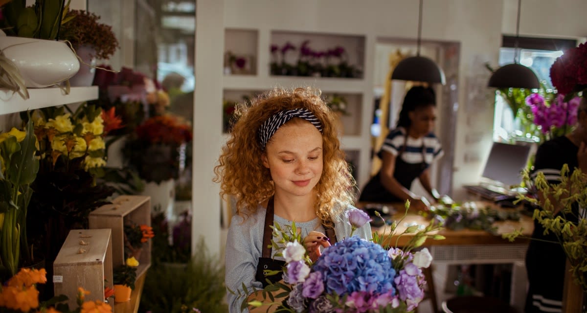 Woman arranging colorful fresh flowers in urban flower shop surrounded by blooms