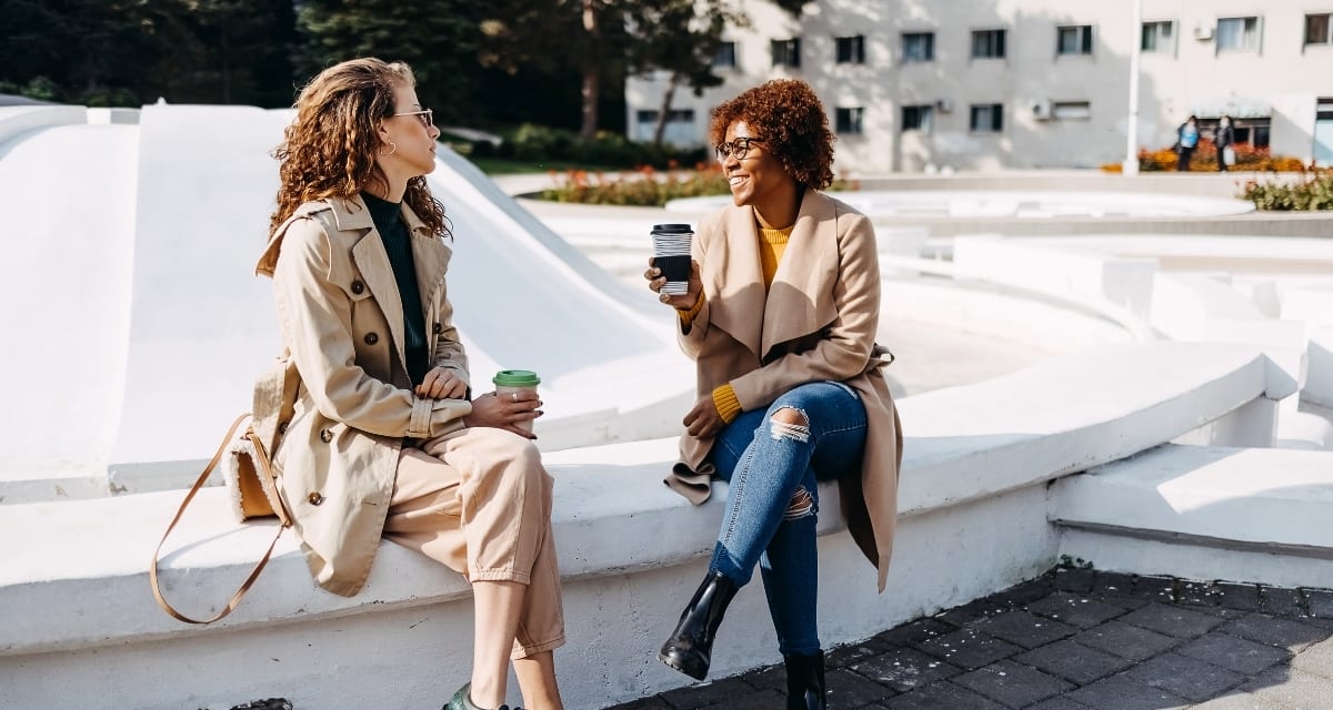 Two people engaged in friendly conversation, smiling and making eye contact outdoors