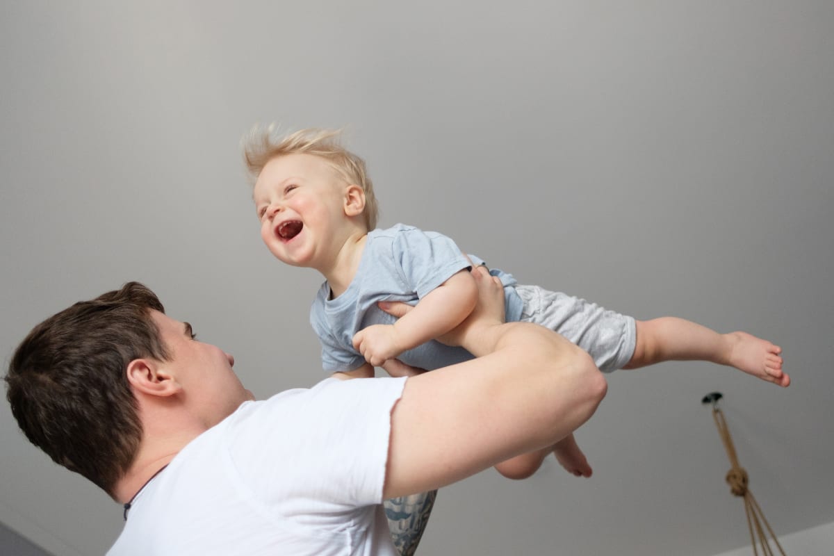Father safely tossing smiling baby onto couch cushion during supervised play session