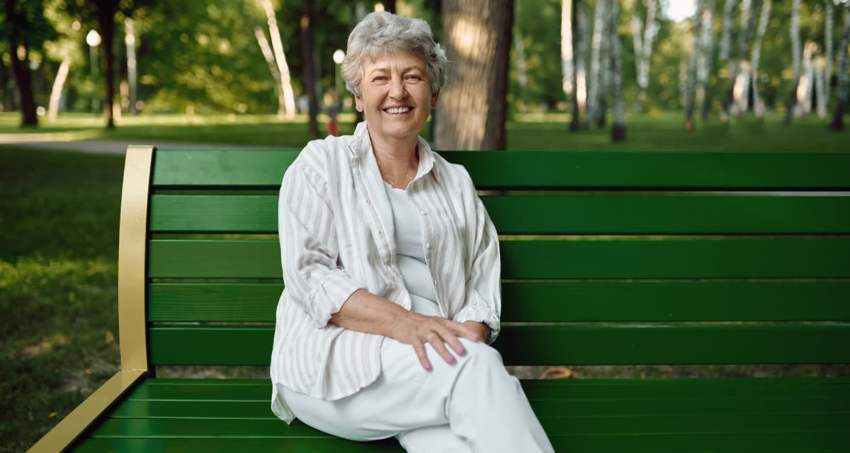 Senior volunteer sitting on outdoor bench talking with younger person in supportive conversation