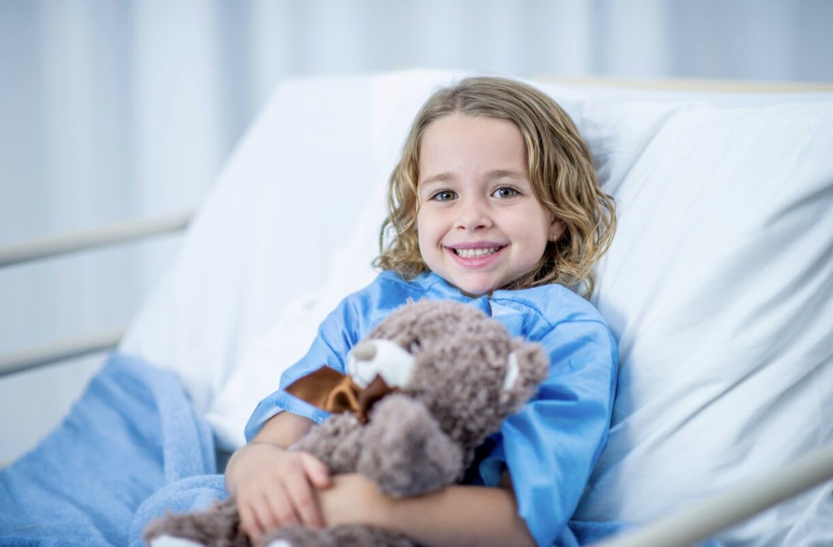 Children in hospital wearing colorful Toy Story character-themed hospital gowns while playing with toys