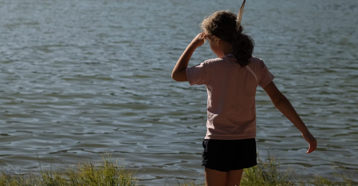 Young girl holding a gold wedding ring near a lake shoreline in Minnesota