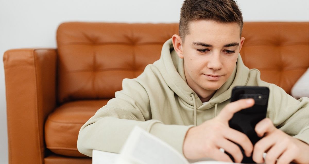 Teenager holding smartphone looking at screen with concentrated expression while texting