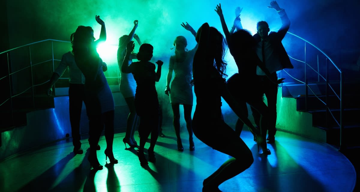 Disco ball hanging in retro nightclub with people of multiple generations dancing together