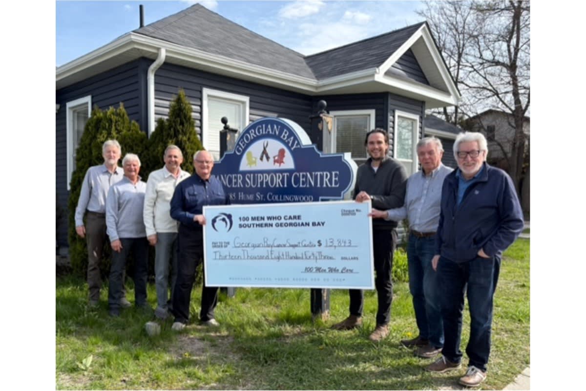 Group of men gathered together presenting large donation check to cancer support centre representatives