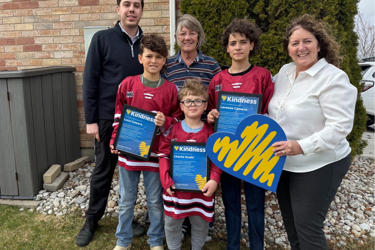 Three young boys holding hockey jerseys standing with elderly woman Joan Knox smiling outdoors