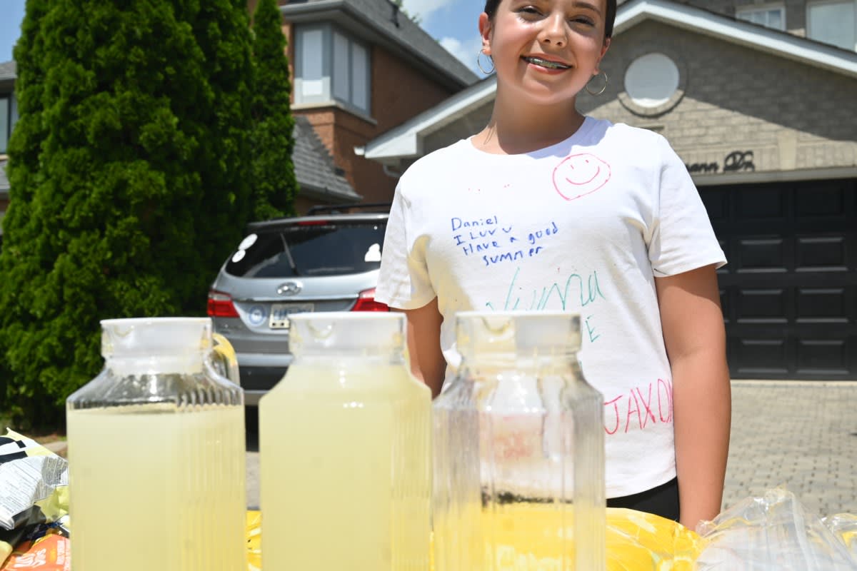Young girl smiling behind lemonade stand table with drinks and snacks displayed