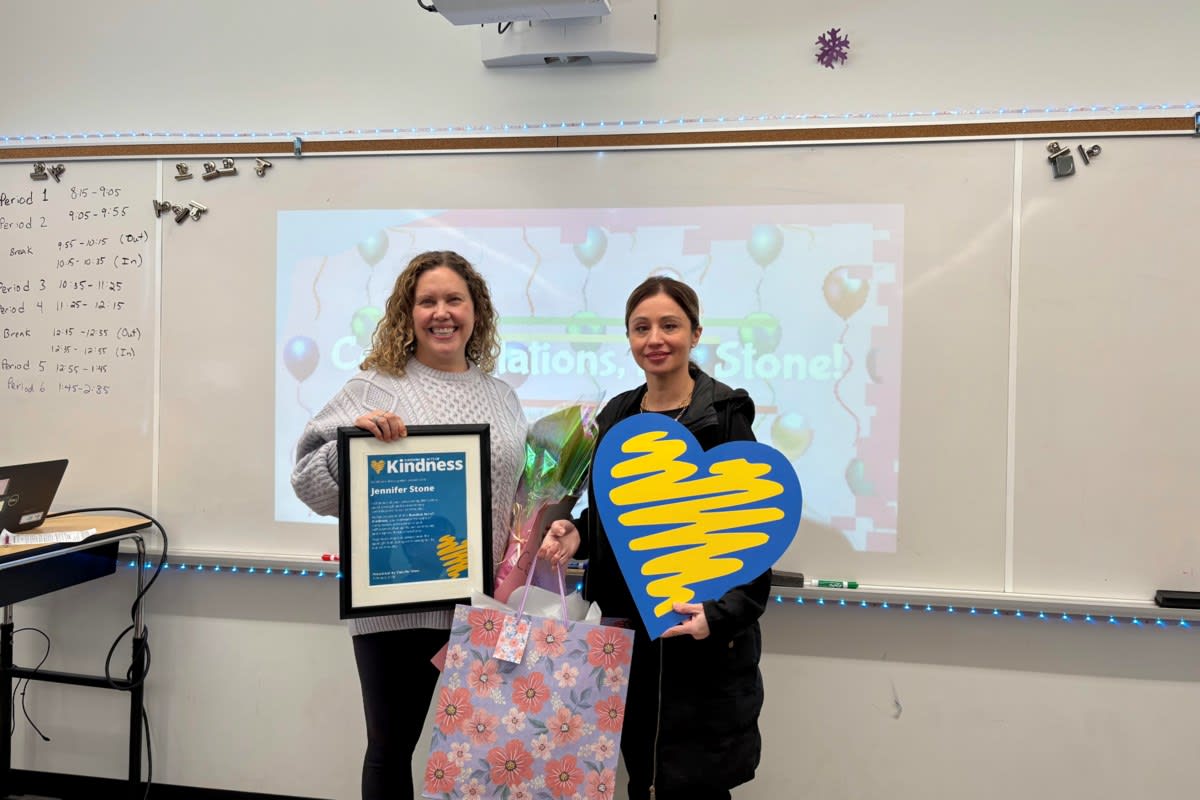 Teacher Jennifer Stone smiling in her classroom surrounded by students and flowers