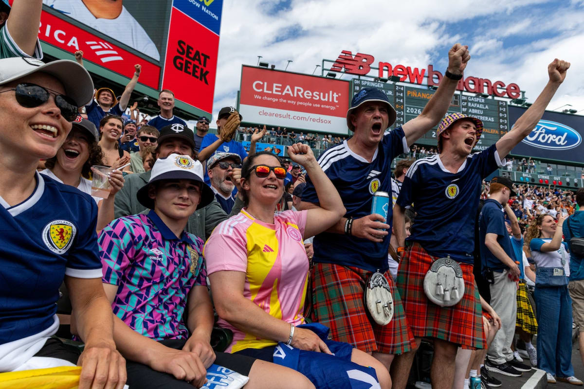 ** Scottish soccer fans in traditional kilts celebrating with drinks at a Boston pub
