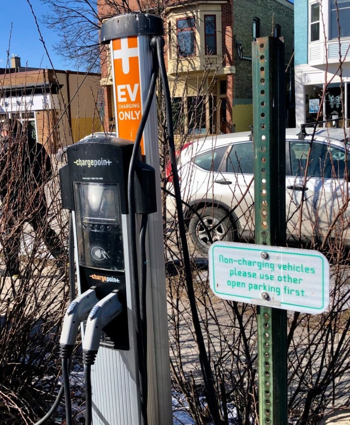 Electric vehicle plugged into charging station in parking lot with business storefront nearby