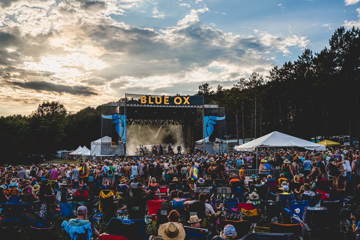 Musicians performing bluegrass music on outdoor stage surrounded by pine trees at Blue Ox Festival