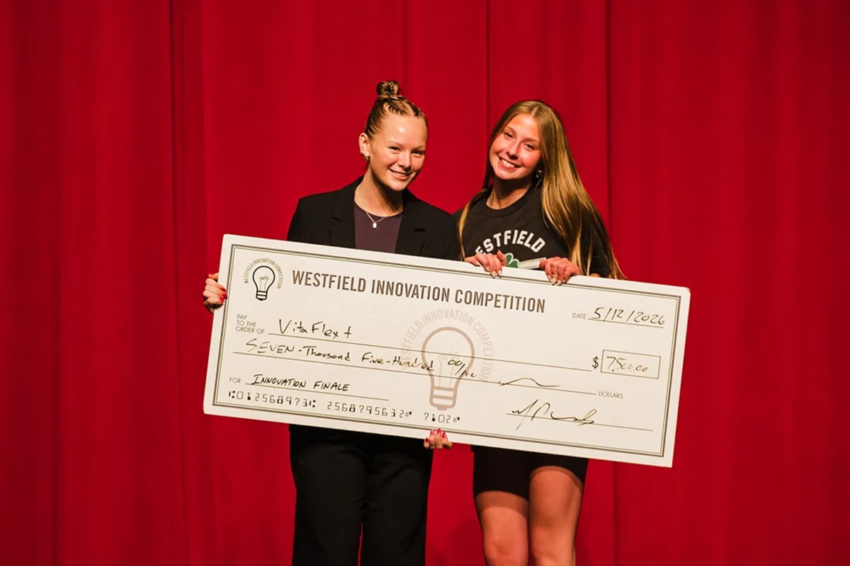 Two high school students holding oversized check at innovation competition award ceremony