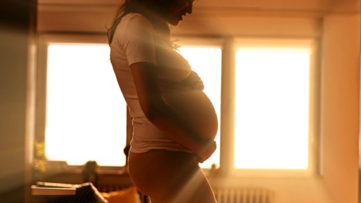 Pregnant woman standing by window in supportive birth centre environment with natural lighting