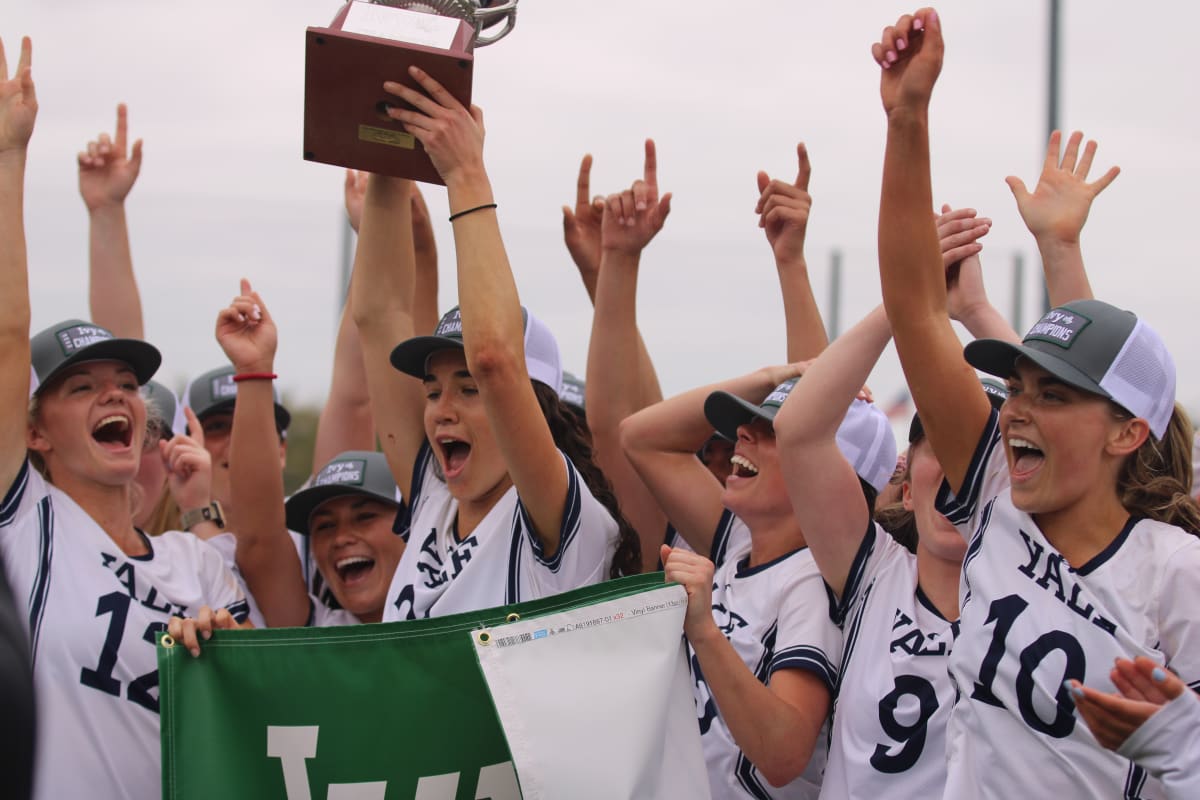 Yale women's lacrosse team celebrating championship victory on field with trophy