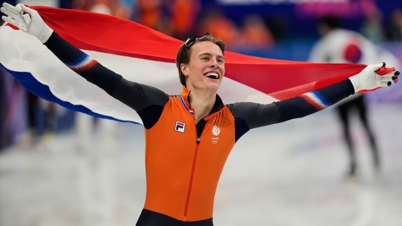 Dutch speedskater Jens van 't Wout celebrating with arms raised on ice rink surrounded by teammates
