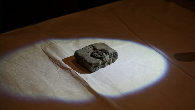 Bronze wheel-shaped cross from medieval Germany held by gloved hand against neutral background