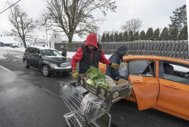 Volunteers loading bags of food into cars at outdoor food bank distribution in snowy conditions