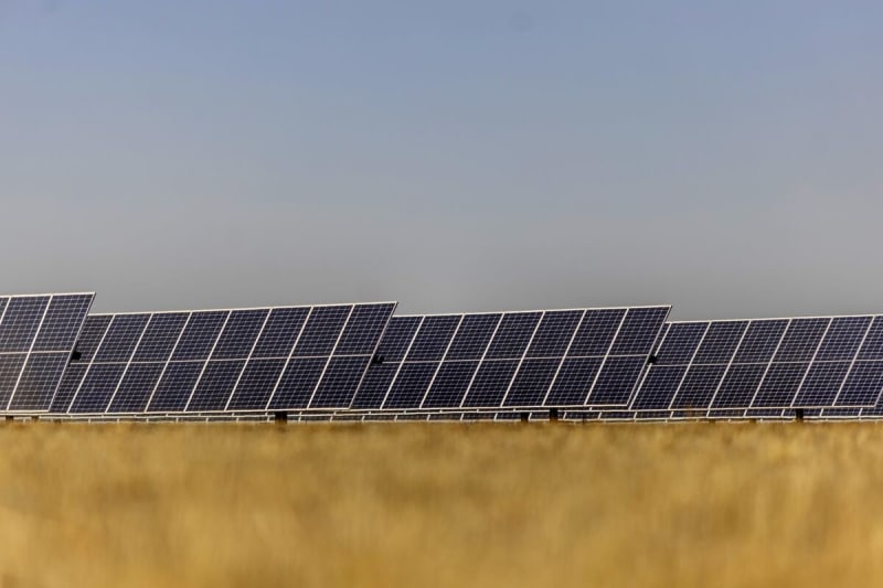 Large solar panel installation reflecting sunlight across African landscape under clear blue sky