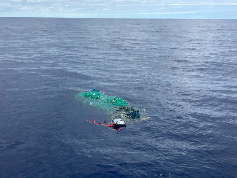 Researcher on boat handing GPS tracking buoy to yacht race captain for ocean cleanup mission