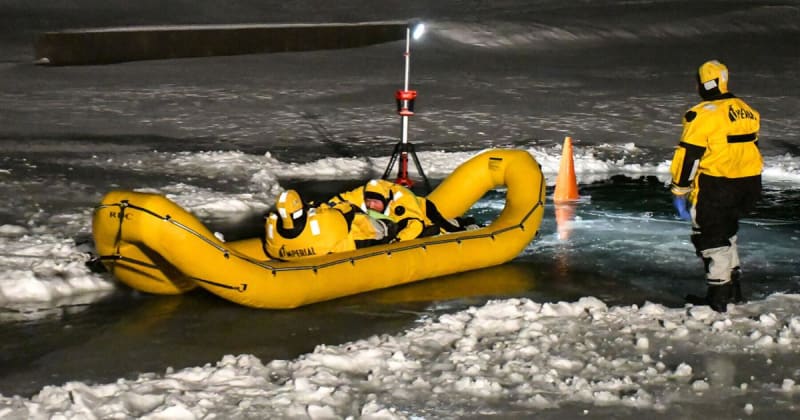 Firefighters in red ice rescue suits training on frozen pond with inflatable rescue craft