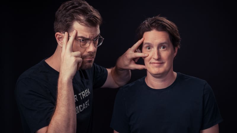 Two podcast hosts smiling while recording at microphones with Star Trek memorabilia visible