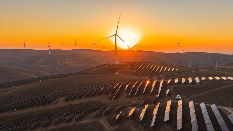Solar panel installation at sunset with wind turbines visible in background