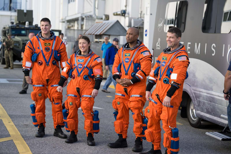 Four Artemis 2 astronauts in blue flight suits stand outside Kennedy Space Center building