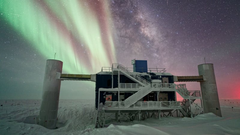 IceCube facility detector strings beneath green Southern Lights at Antarctic South Pole station
