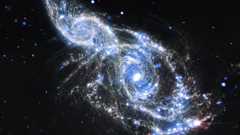 Two spiral galaxies IC 2163 and NGC 2207 with silvery-blue arms embracing in space, captured by Webb and Chandra telescopes
