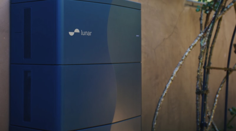 Modern home battery storage system mounted on residential garage wall with solar panels visible