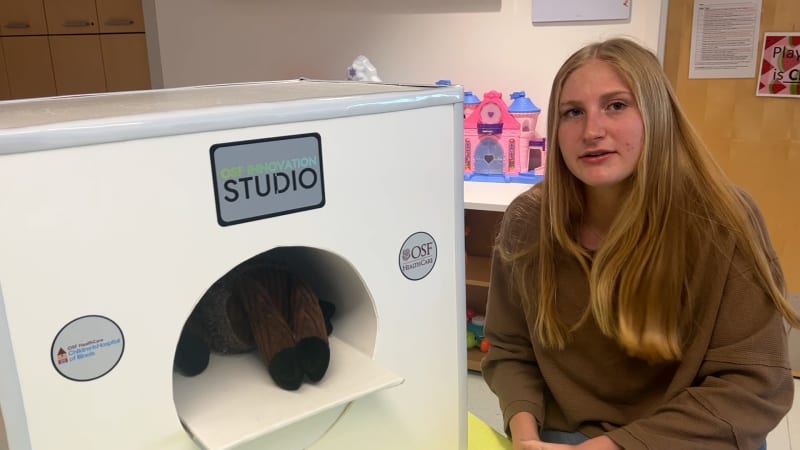Teen cancer survivor Savannah Jost standing beside child-sized toy MRI machine at Illinois children's hospital