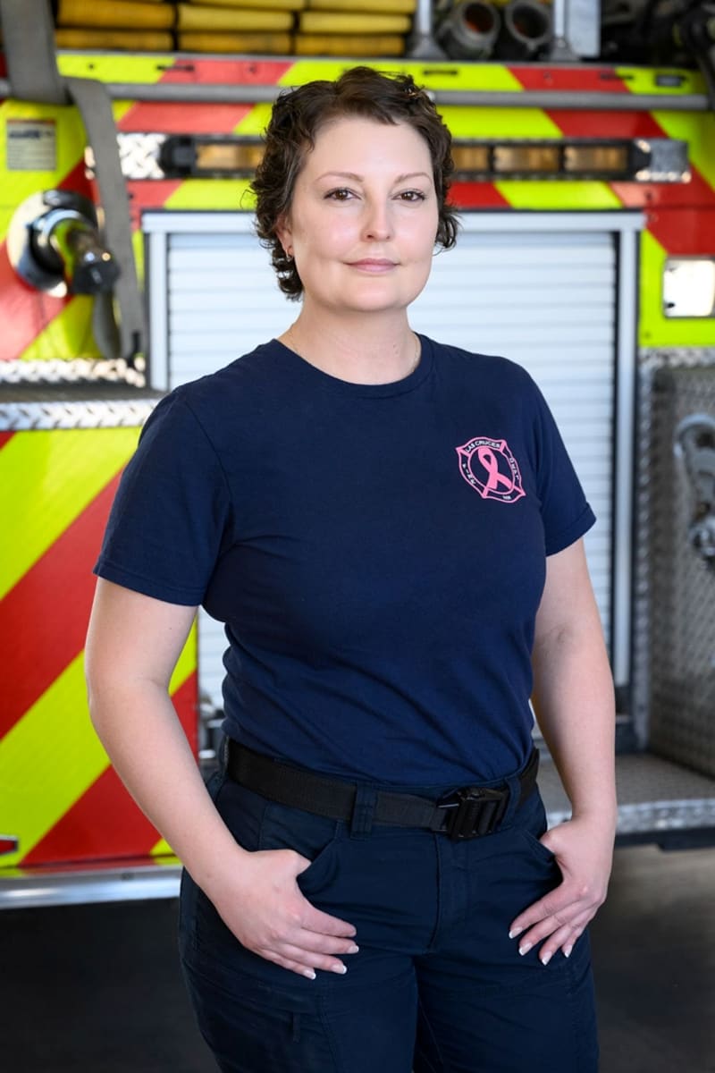 Firefighter Nicole Walls in uniform holding her helmet at Las Cruces fire station