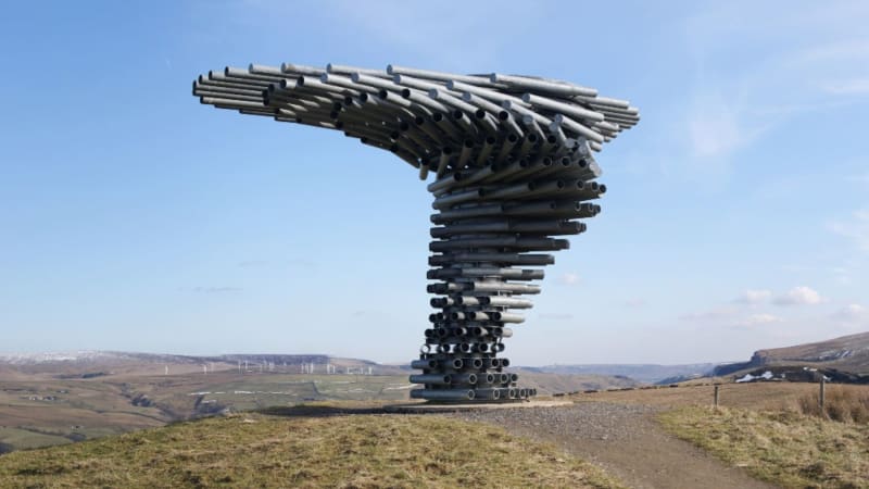 Steel pipe sculpture resembling twisted tree on English hillside creating music from wind