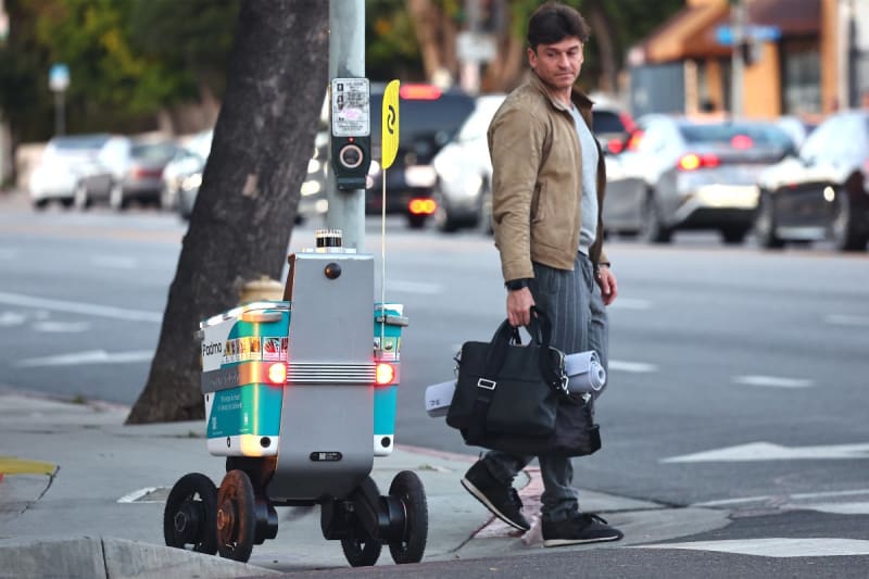 Robot wrangler worker assisting small wheeled delivery robot on urban Los Angeles sidewalk