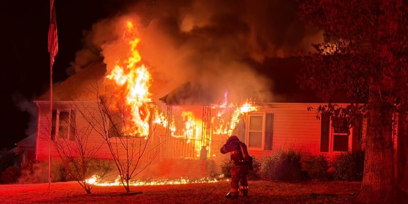 Firefighters battling house fire at night while community members watch, representing neighborhood heroism and emergency response