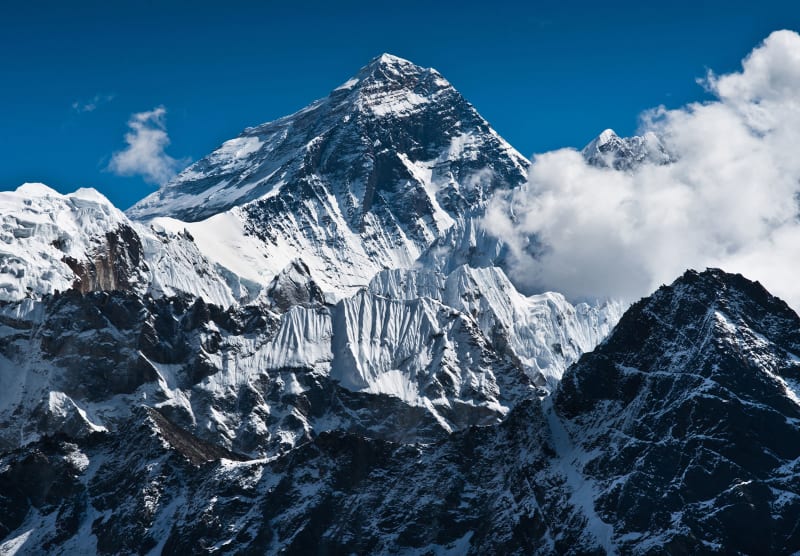 Mountain climber ascending snowy Himalayan peak against blue sky without oxygen equipment