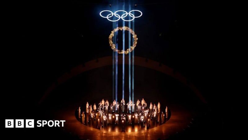 British athletes waving flags at Verona closing ceremony with Olympic rings illuminated behind them