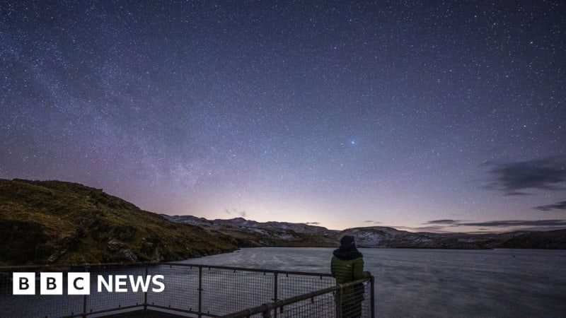 People lying on blankets gazing up at star-filled night sky in rural Welsh countryside