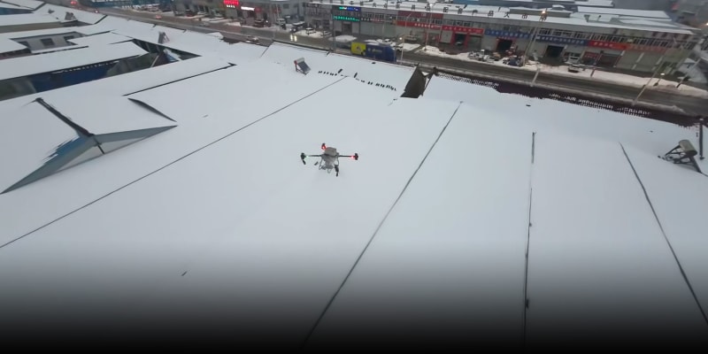 Drone hovering above snow-covered greenhouse, blasting away accumulated snow with high-powered motors