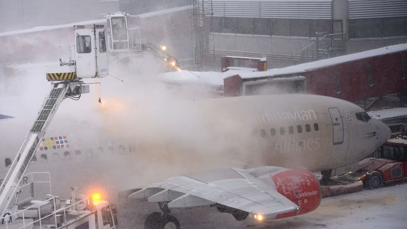 Happy travelers consulting information at modern European airport during winter, displaying confidence and preparedness despite weather conditions.