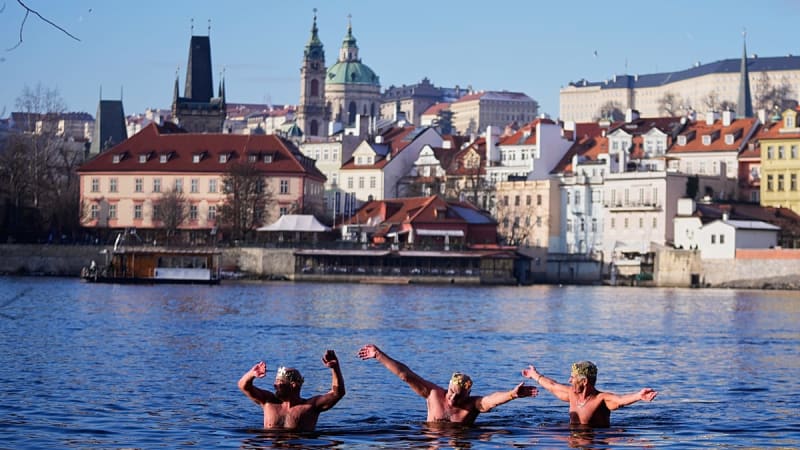 Swimmers in crowns diving into icy Vltava River near Prague's Charles Bridge during traditional Three Kings celebration