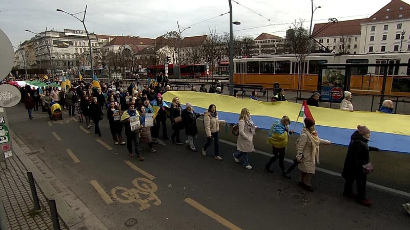 People gathering at outdoor demonstration in Budapest holding signs supporting Ukraine