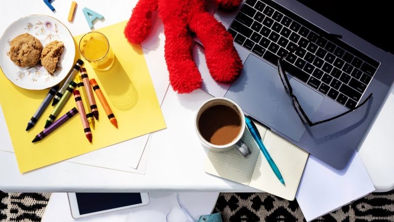 Parent smiling at phone while child plays nearby, morning sunlight streaming through kitchen window