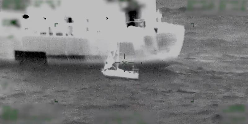 Small sailboat with tattered sails being tethered to large tanker during rough ocean rescue operation