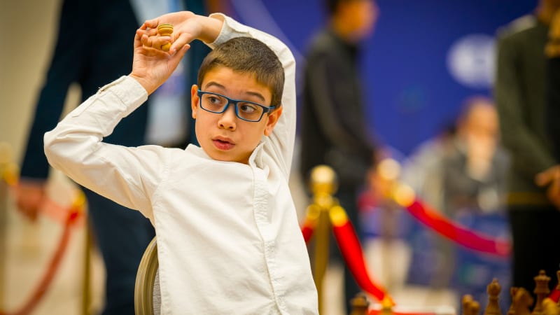 Young chess prodigy Faustino Oro competing at international chess championship tournament with focused concentration