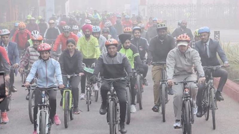 Working-class cyclist riding steel-frame bicycle through busy Delhi traffic on arterial road