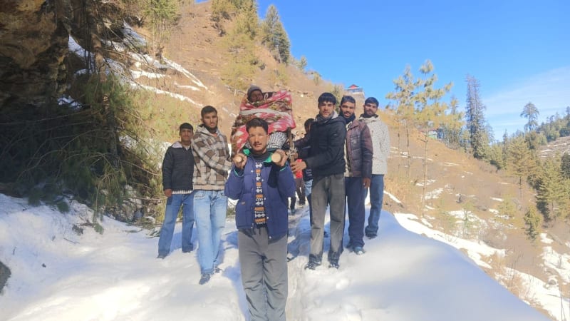 Group of men carrying elderly patient on wooden chair through deep snow in Himalayan mountains