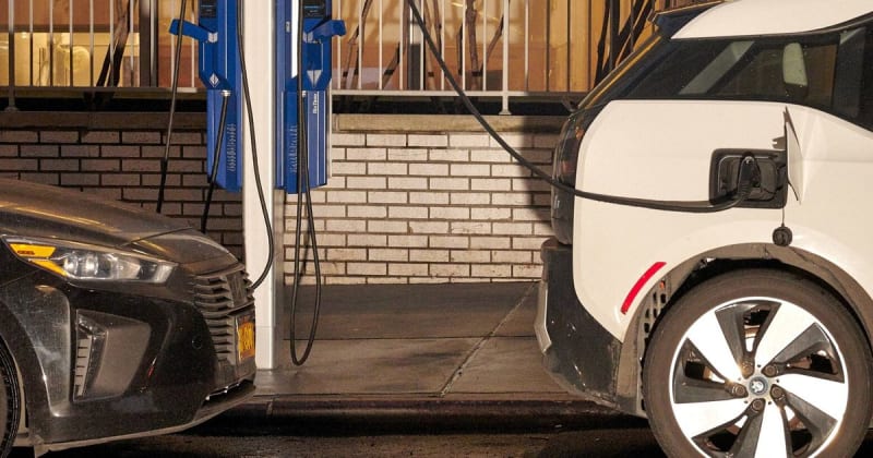Two electric vehicles charging at public charging stations with power cables connected
