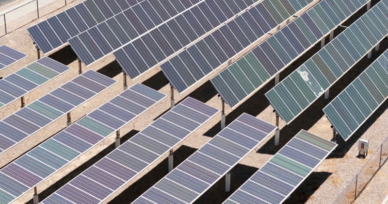Aerial view of large solar panel array stretching across open land in bright sunlight