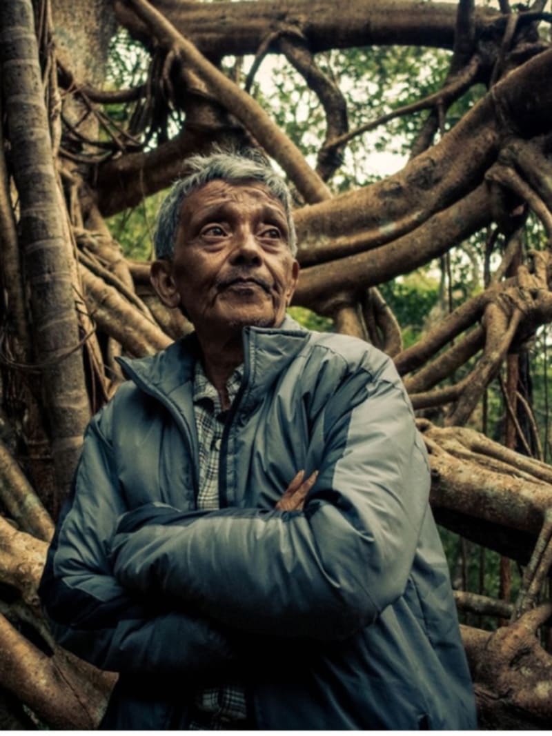 Hally War standing on living root bridge made from intertwined tree roots in Meghalaya forest
